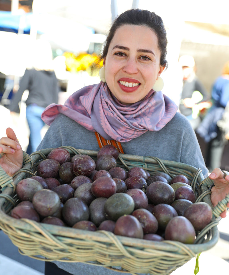 Uli Nasibova smiling and holding up a basket of fresh passion fruit 